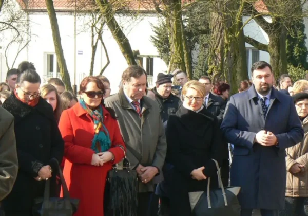 Grupa uczestników Drogi Krzyżowej stoi razem na ulicy w zimowych płaszczach, z torbami u boku.