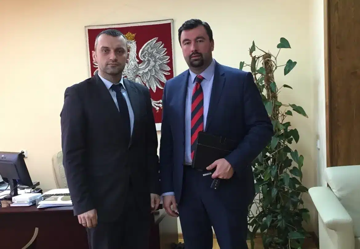 Starosta Płocki i jego rozmówca pozują do zdjęcia w biurze, w tle widoczna jest herbowa flaga i roślina doniczkowa.