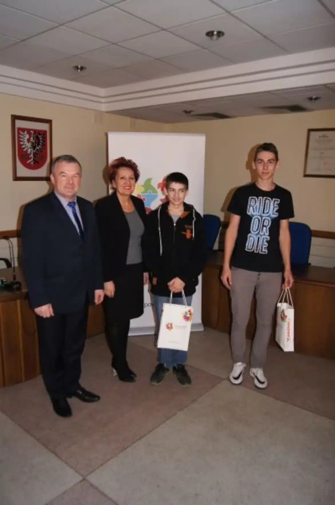 Na zdjęciu widoczni są uczestnicy lekcji wychowania obywatelskiego w Starostwie, stojący obok przedstawicieli urzędów, trzymający torby z upominkami.