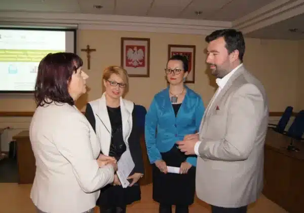 Na zdjęciu widoczne jest spotkanie seminaryjne dla Jednostek Organizacyjnych Pomocy Społecznej na Mazowszu, w którym uczestniczy czterech osób rozmawiających w sali konferencyjnej.