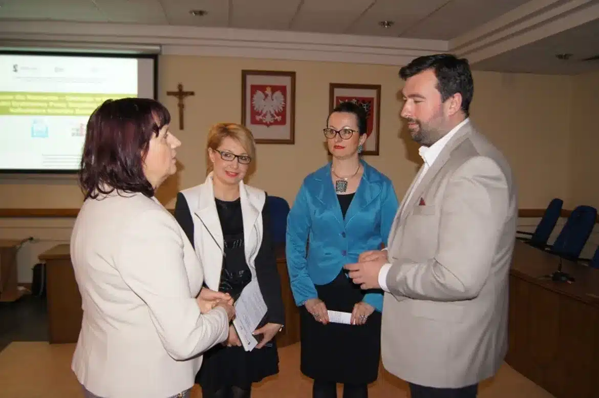 Na zdjęciu widoczne jest spotkanie seminaryjne dla Jednostek Organizacyjnych Pomocy Społecznej na Mazowszu, w którym uczestniczy czterech osób rozmawiających w sali konferencyjnej.