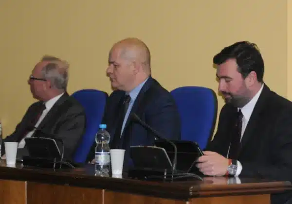 Na zdjęciu trzej mężczyźni siedzą przy stole podczas debaty społecznej, w tle widoczne są niebieskie krzesła.