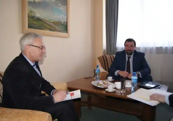 Spotkanie dotyczące spraw drogowych u Starosty, z dwoma mężczyznami siedzącymi przy stole, z notatkami i napojami.