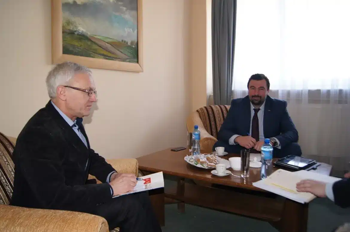 Spotkanie dotyczące spraw drogowych u Starosty, z dwoma mężczyznami siedzącymi przy stole, z notatkami i napojami.