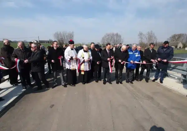 Na zdjęciu widoczna jest grupa mężczyzn, w tym duchowni i samorządowcy, trzymających wstęgę podczas ceremonii otwarcia przegrody dolinowej w Stanownie.