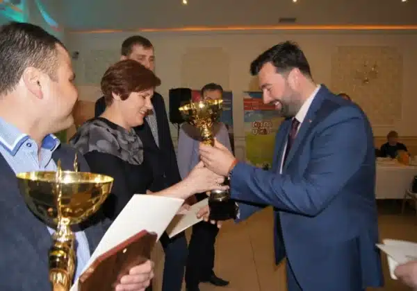 Na zdjęciu widać uśmiechniętych uczestników spotkania z hodowcami bydła mlecznego, którzy wręczają sobie puchary i dyplomy w eleganckiej sali.