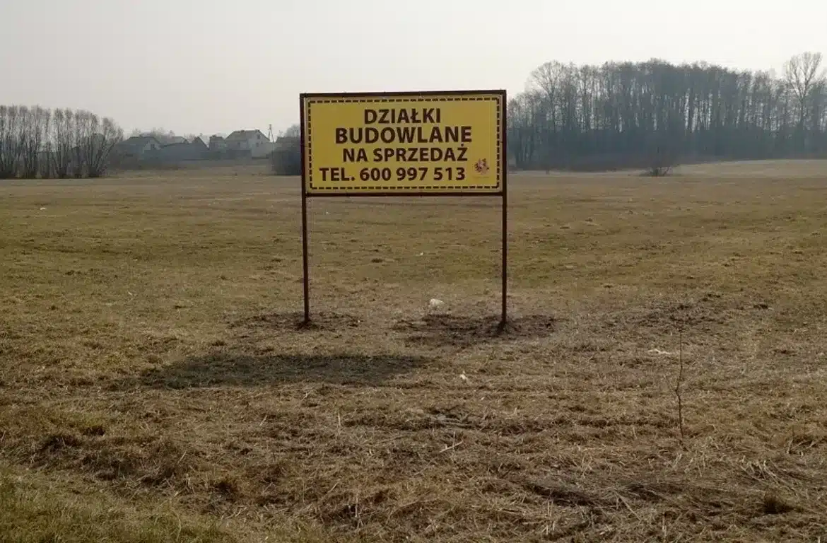 Na zdjęciu widoczny jest znak informujący o sprzedaży działek budowlanych w Miszewie Murowanym, umieszczony na pustym, trawiastym terenie.