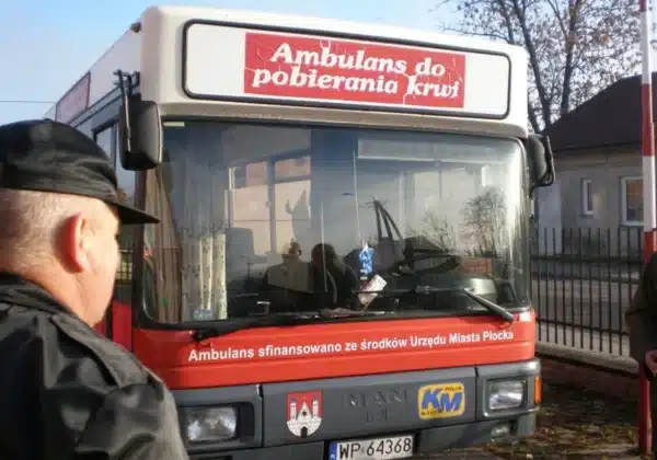Na zdjęciu widoczny jest ambulans do pobierania krwi z napisem „Ambulans do pobierania krwi” oraz osoby zgromadzone wokół niego, w kontekście akcji pomocy chorej na białaczkę.