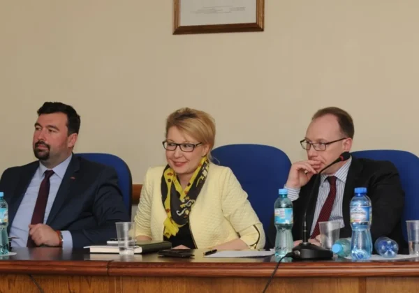 Na zdjęciu przedstawiono trzech uczestników IV Sesji Rady Powiatu Płockiego, siedzących przy stole z napojami i notatnikami.