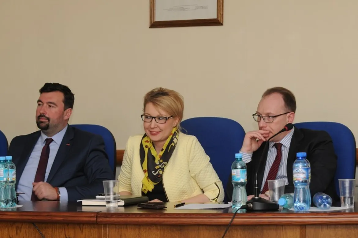 Na zdjęciu przedstawiono trzech uczestników IV Sesji Rady Powiatu Płockiego, siedzących przy stole z napojami i notatnikami.