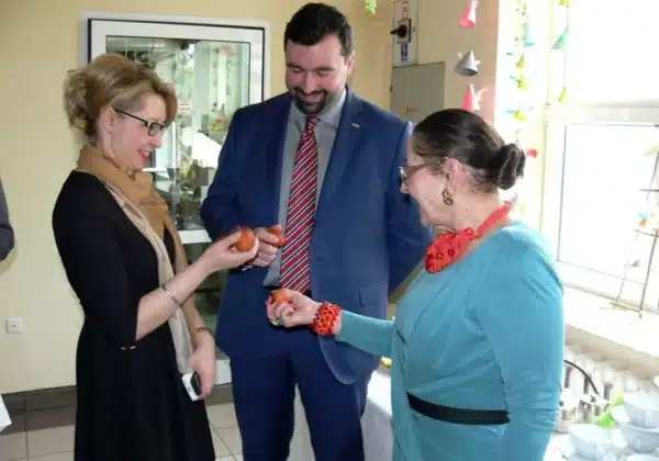 Na zdjęciu widać trzy osoby, które z uśmiechami trzymają kolorowe pisanki podczas spotkania wielkanocnego w Domu Pomocy Społecznej w Zakrzewie.