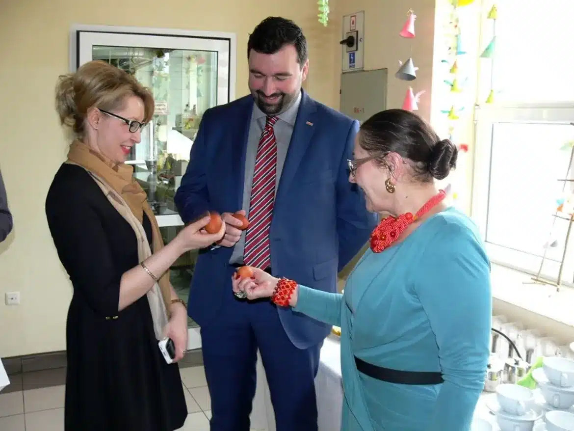 Na zdjęciu widać trzy osoby, które z uśmiechami trzymają kolorowe pisanki podczas spotkania wielkanocnego w Domu Pomocy Społecznej w Zakrzewie.