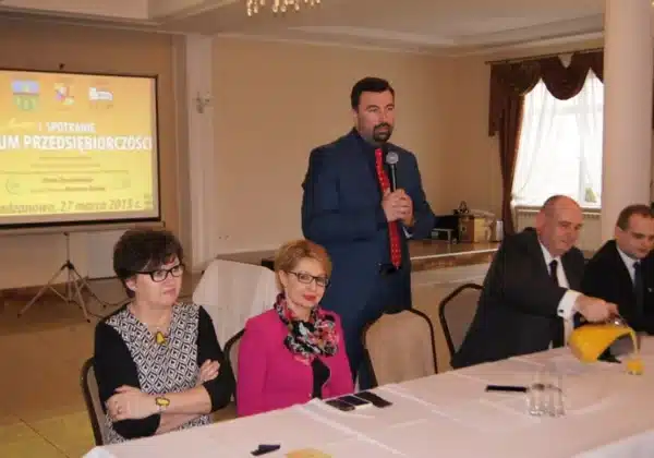 Uczestnicy I Spotkania Forum Przedsiębiorczości w Radzanowie rozmawiają przy jednym stole, a jeden z mężczyzn przemawia do zgromadzonych.