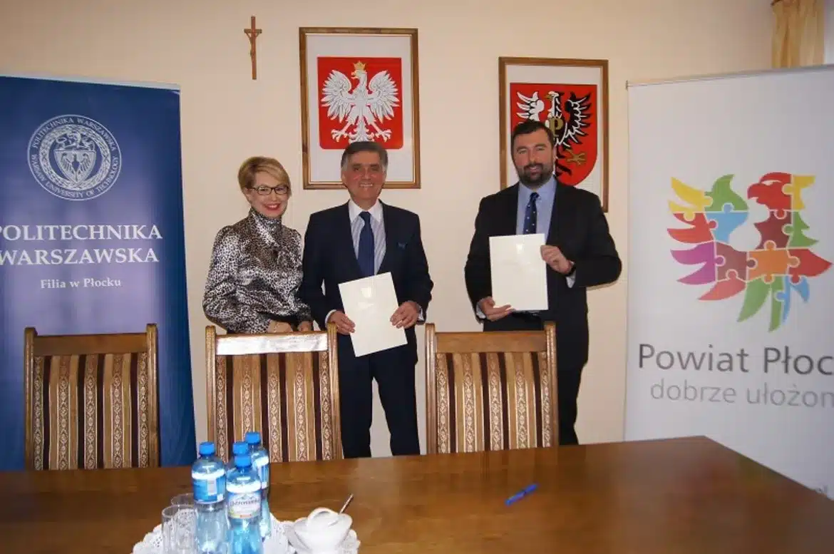 Trzy osoby, przedstawiciele Powiatu Płockiego oraz Politechniki Warszawskiej Filia w Płocku, uśmiechają się, trzymając dokumenty potwierdzające zawarcie porozumienia o współpracy.