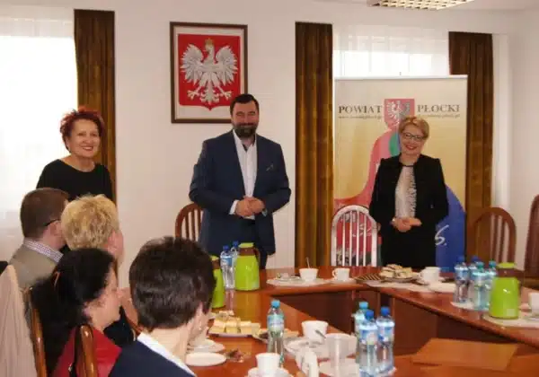Spotkanie integrujące organizacje pozarządowe działające w sferze publicznej na terenie powiatu płockiego, z widocznymi uczestnikami przy stole oraz banerem powiatu w tle.
