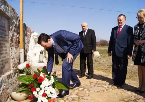 Uroczystość upamiętniająca ofiary katastrofy smoleńskiej, z udziałem kilku osób składających kwiaty przy pomniku.