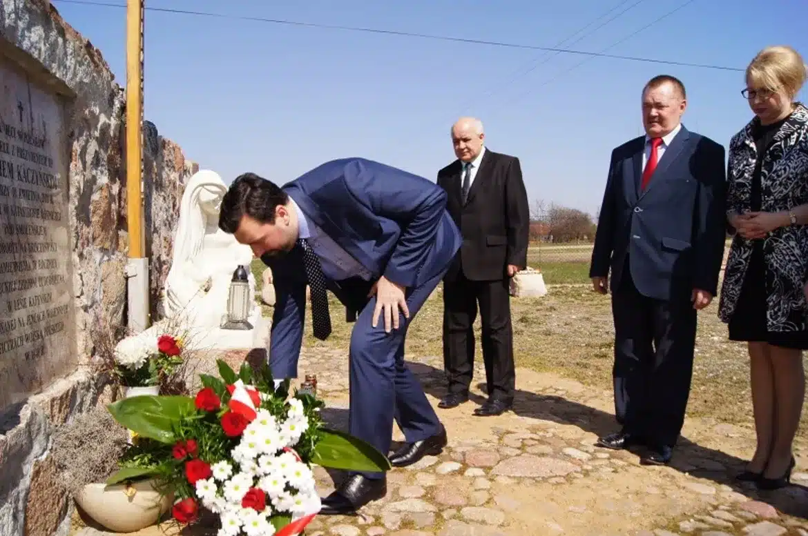 Uroczystość upamiętniająca ofiary katastrofy smoleńskiej, z udziałem kilku osób składających kwiaty przy pomniku.