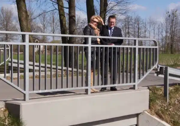 Na zdjęciu widać dwoje ludzi stojących na balustradzie mostu, obserwujących okolicę w słoneczny dzień.