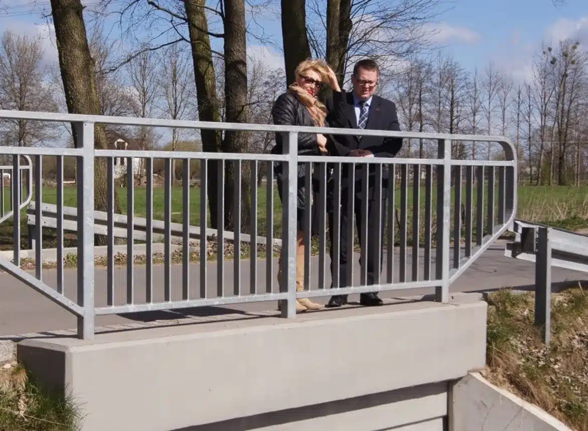 Na zdjęciu widać dwoje ludzi stojących na balustradzie mostu, obserwujących okolicę w słoneczny dzień.