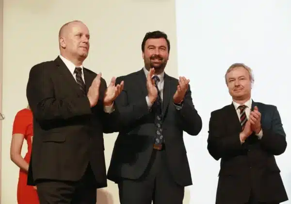 Uroczystość wręczenia nagród w konkursie „Z Tumskiego Wzgórza”, na której obecni są uśmiechnięci mężczyźni w garniturach, oklaskujący wydarzenie.