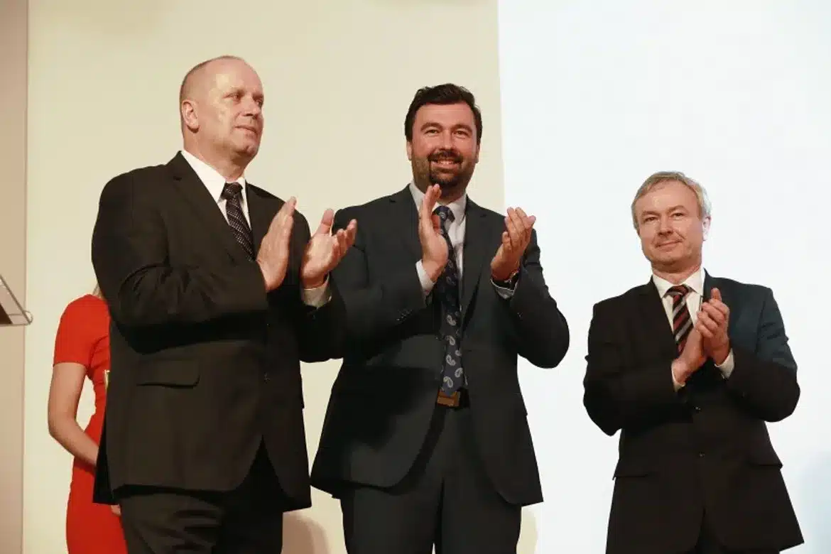 Uroczystość wręczenia nagród w konkursie „Z Tumskiego Wzgórza”, na której obecni są uśmiechnięci mężczyźni w garniturach, oklaskujący wydarzenie.