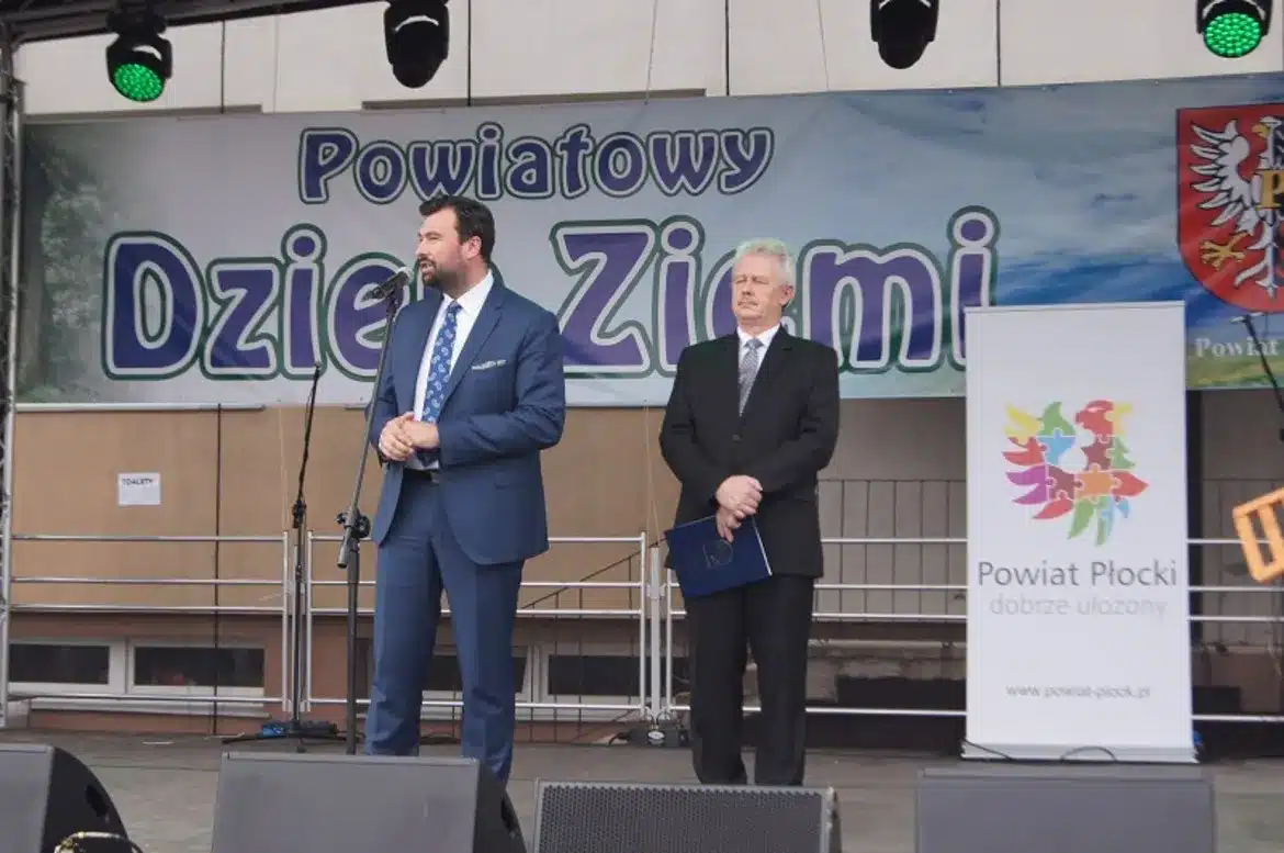 Na zdjęciu przedstawiono dwóch mężczyzn stojących na scenie podczas XVI Powiatowego Dnia Ziemi w Słubicach, z banerem w tle.