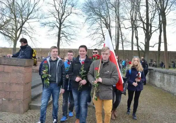 Młodzież z flagą Polski oraz kwiatami w rękach uczestniczy w obchodach 70. rocznicy wyzwolenia KL Ravensbrück.
