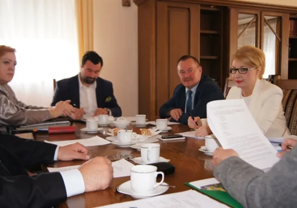 Grupa urzędników Zarządu Powiatu w Płocku siedzi przy stole w biurze podczas spotkania, omawiając dokumenty i prowadząc notatki przy filiżankach kawy i talerzach z przekąskami.