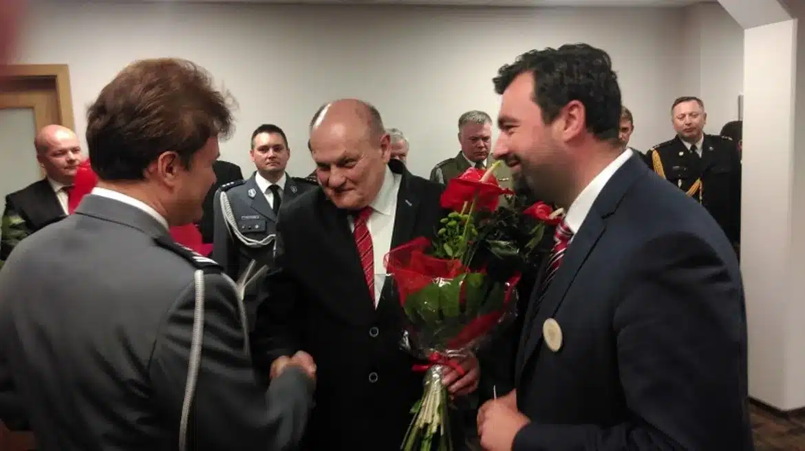 Na zdjęciu przedstawiono emocjonalną chwilę pożegnania Komendanta Miejskiego Policji w Płocku, który odchodzi na emeryturę, w otoczeniu współpracowników i kwiatów.