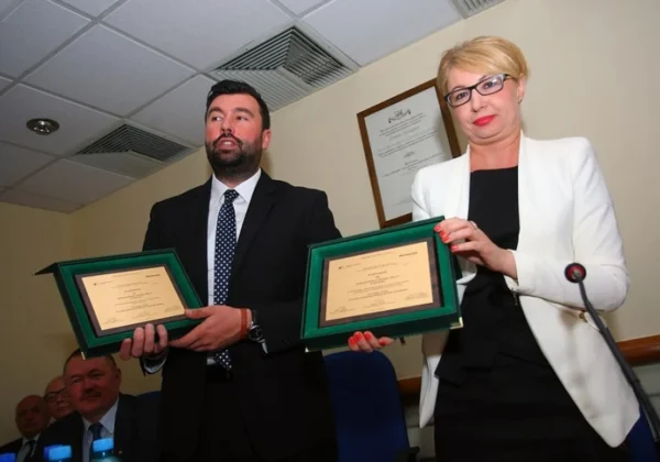 Dwóch urzędników Powiatowego Urzędu Pracy w Płocku prezentuje dyplomy w zielonych ramach podczas uroczystości wyróżnień.