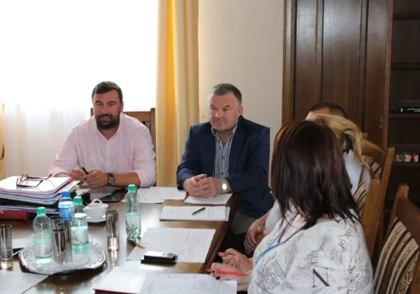 Grupa osób siedzi przy stole w sali konferencyjnej podczas posiedzenia Zarządu Powiatu, otoczeni dokumentami, notatkami i butelkami wody.