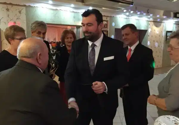 Na zdjęciu przedstawiono uczestników corocznego Balu Seniorów, którzy witają się i rozmawiają w eleganckiej sali.