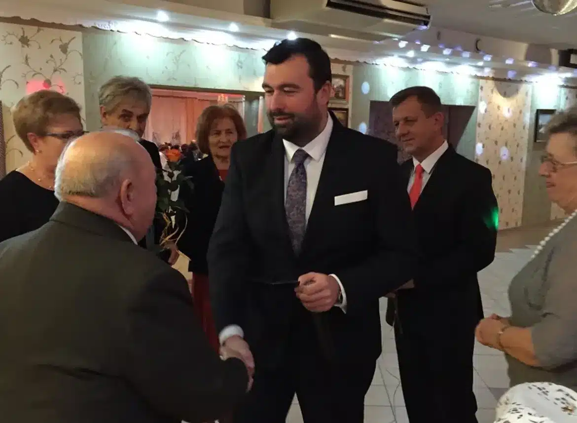 Na zdjęciu przedstawiono uczestników corocznego Balu Seniorów, którzy witają się i rozmawiają w eleganckiej sali.