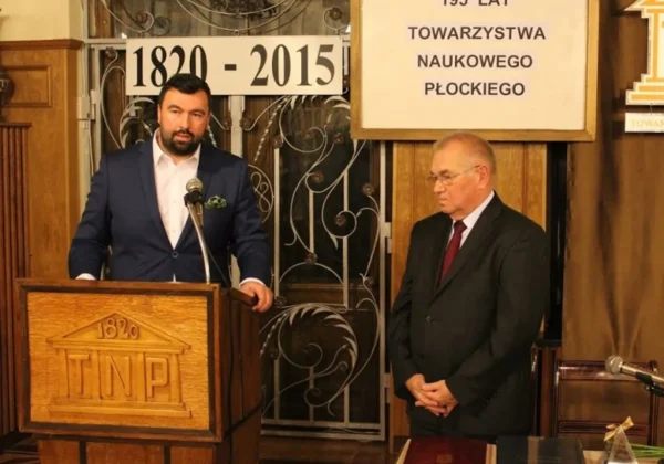 Zdjęcie przedstawia dwóch mężczyzn podczas uroczystości związanej z 195-leciem Towarzystwa Naukowego Płockiego, z jednym z nich mówiącym do mikrofonu.