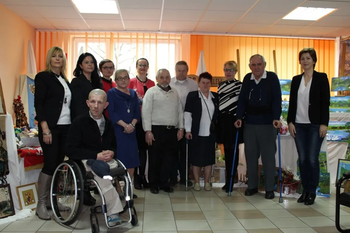 Grupa mieszkańców Domu Pomocy Społecznej w Koszelewie w towarzystwie pracowników Starostwa Powiatowego w Płocku na wspólnej fotografii w sali urzędowej.