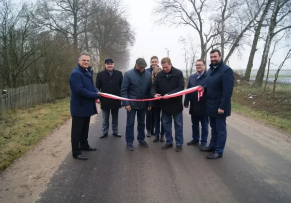 Mężczyźni w garniturach i płaszczach odbierają technicznie przebudowaną drogę, trzymając w rękach biało-czerwoną wstęgę.