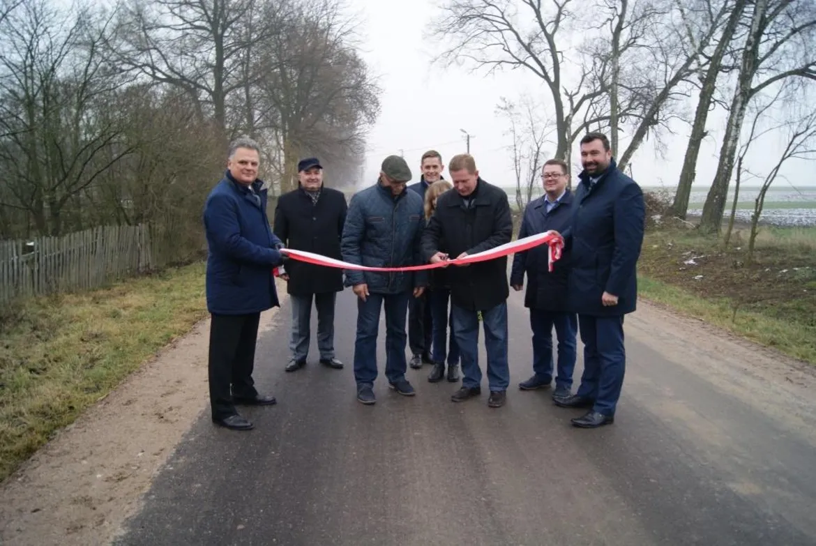 Mężczyźni w garniturach i płaszczach odbierają technicznie przebudowaną drogę, trzymając w rękach biało-czerwoną wstęgę.