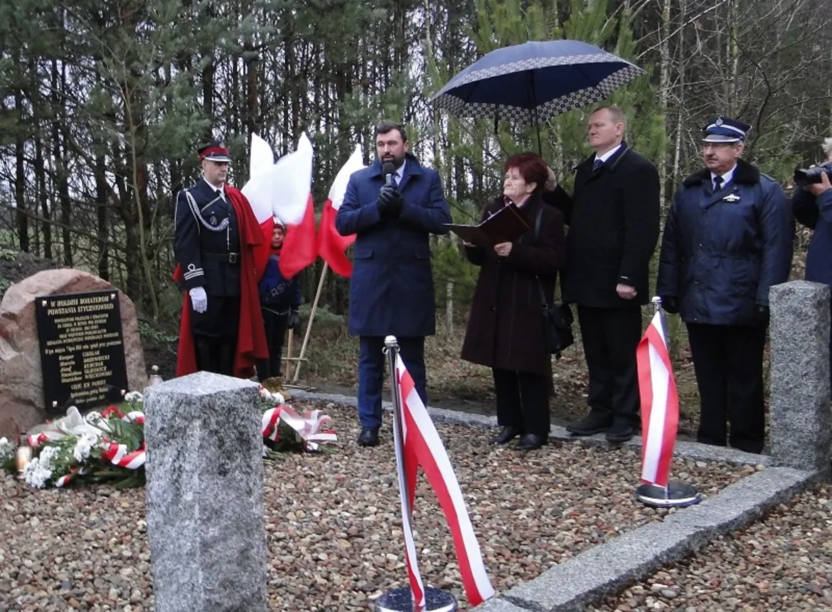 Uroczystość odsłonięcia kopca Bohaterów Powstania Styczniowego z udziałem lokalnych władz i mieszkańców, przy dźwiękach polskiej flagi i zaopatrzonych w parasole mówców.