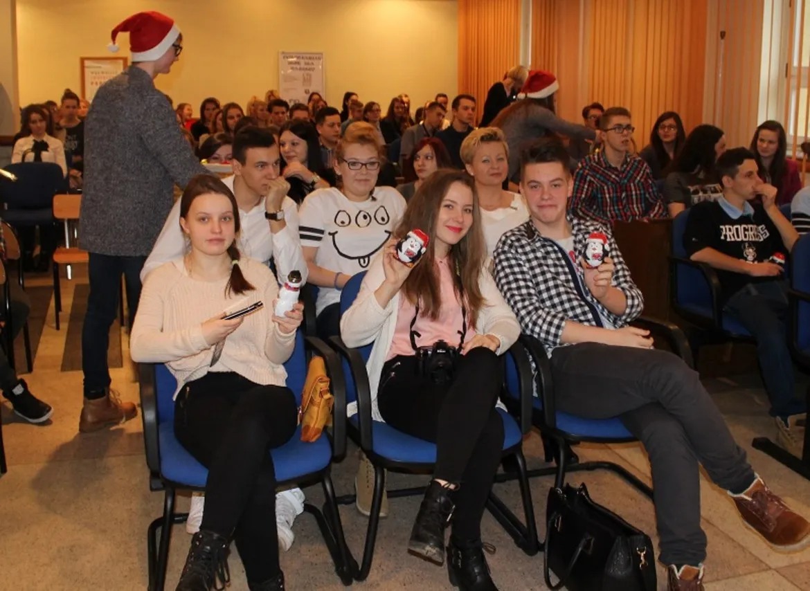 Na zdjęciu widać młodych ludzi siedzących na sali podczas gali wolontariatu „Wolontariat jest dla każdego”, trzymujących w rękach przedmioty z wizerunkiem Mikołaja.