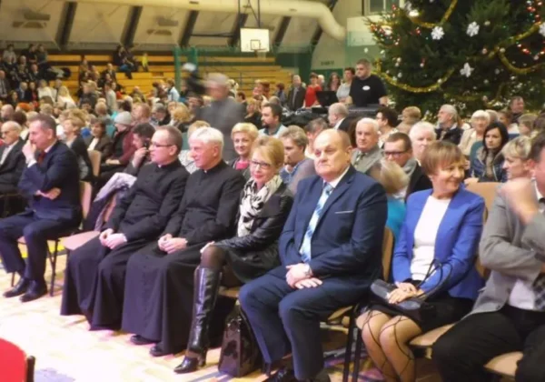 Na zdjęciu widać grupę ludzi siedzących na wydarzeniu gminnym w Łącku, z bożonarodzeniową choinką w tle.
