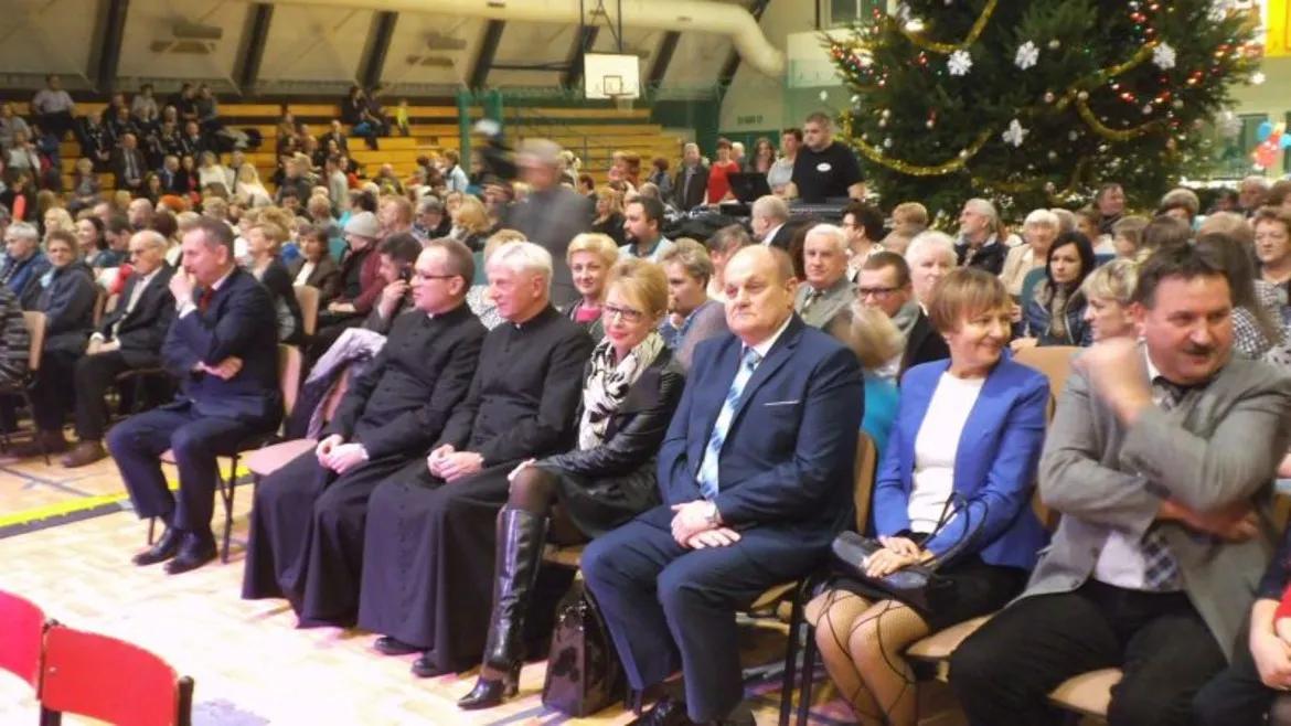 Na zdjęciu widać grupę ludzi siedzących na wydarzeniu gminnym w Łącku, z bożonarodzeniową choinką w tle.