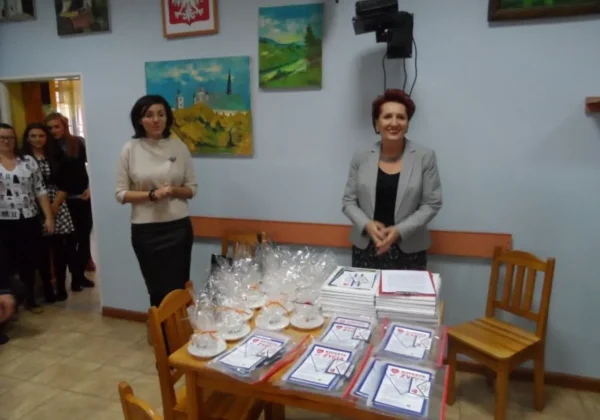 W spotkaniu na temat „Koperty Życia” uczestniczą dwie kobiety, podczas gdy zebrani słuchają o inicjatywie mającej na celu wsparcie osób potrzebujących.