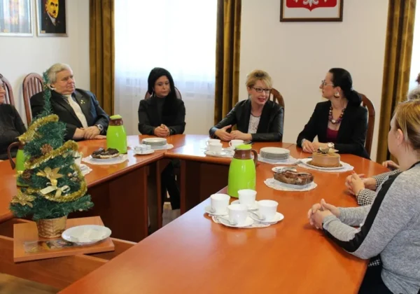 Spotkanie członków Powiatowej Społecznej Rady ds. Osób Niepełnosprawnych przy stole, na którym znajdują się napoje i słodkości, w otoczeniu dekoracji świątecznych.
