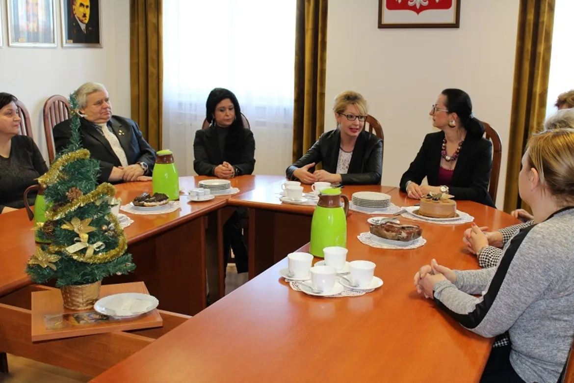 Spotkanie członków Powiatowej Społecznej Rady ds. Osób Niepełnosprawnych przy stole, na którym znajdują się napoje i słodkości, w otoczeniu dekoracji świątecznych.