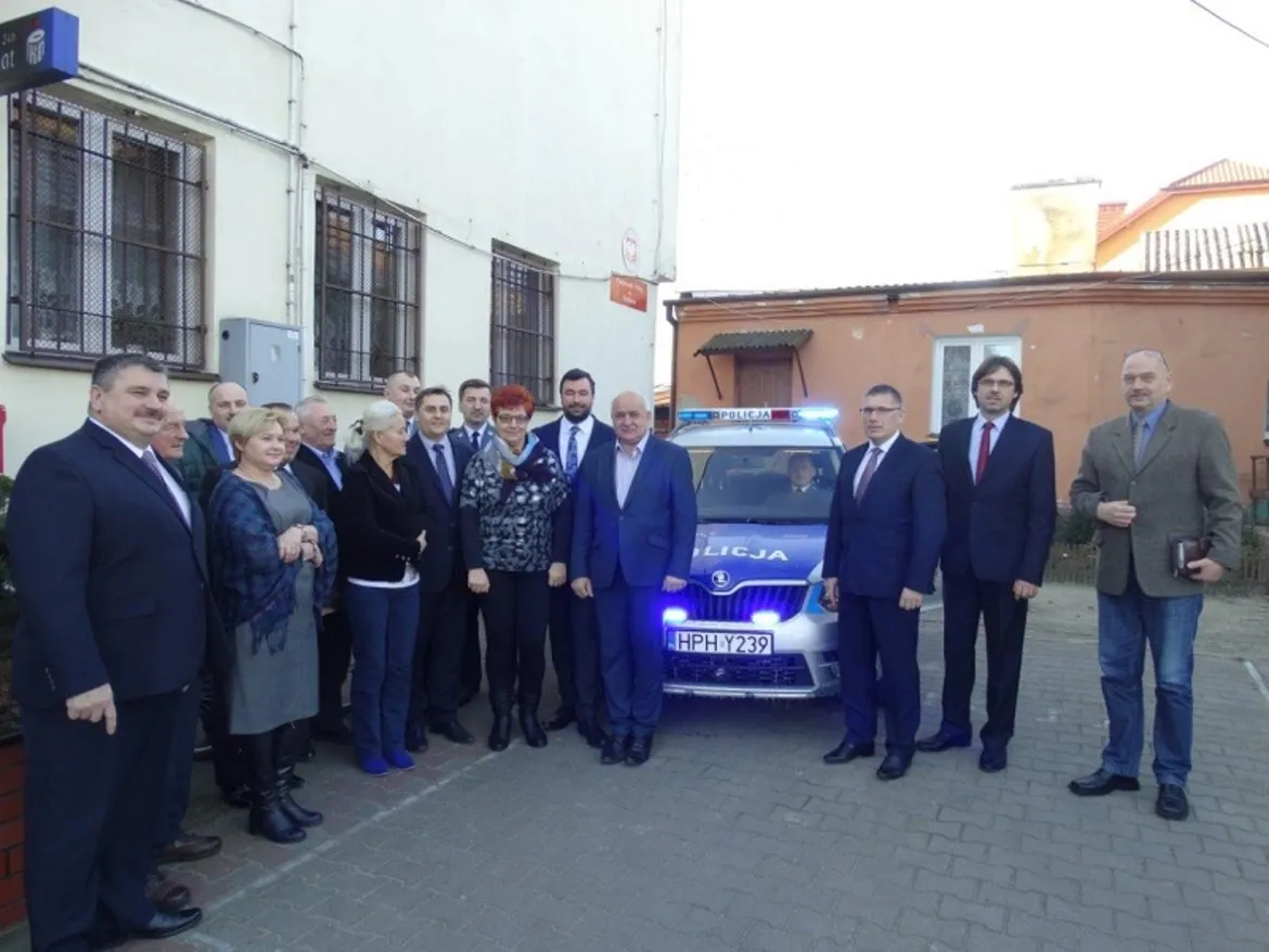 Zdjęcie przedstawia grupę osób stojących przed nowym radiowozem policji, które zostało przekazane dla policjantów z Drobina.