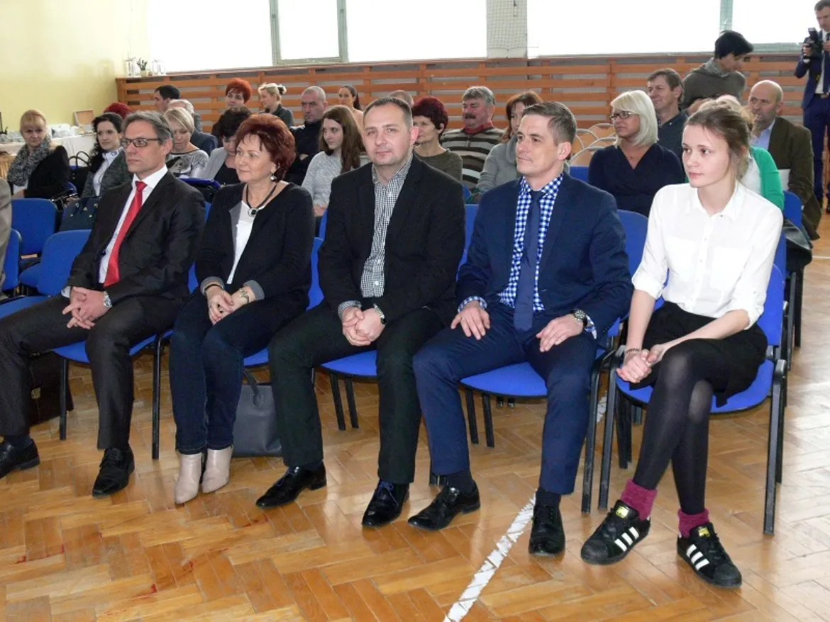 Uczestnicy konferencji „Termomodernizacji obiektów użyteczności publicznej w gminie Bodzanów” siedzą na niebieskich krzesłach, zwracając uwagę na prezentację.