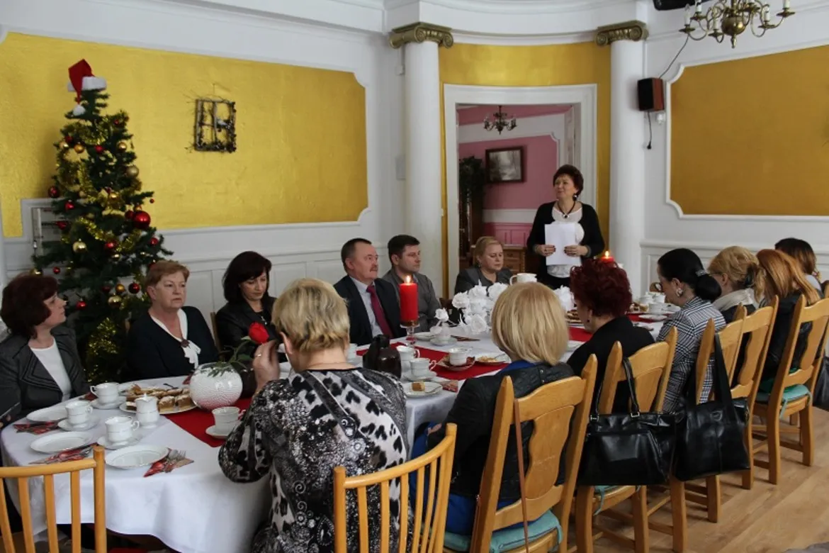 Posiedzenie Komisji do Spraw Społecznych Rady Powiatu Płockiego odbywa się w dekorowanej sali, przy stole zastawionym potrawami, podczas gdy jedna z uczestniczek wygłasza przemówienie.