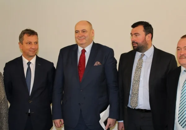 Na zdjęciu grupa mężczyzn w garniturach oraz jedna kobieta, stojących w prostym wnętrzu, dyskutujących na temat podziału województwa mazowieckiego.