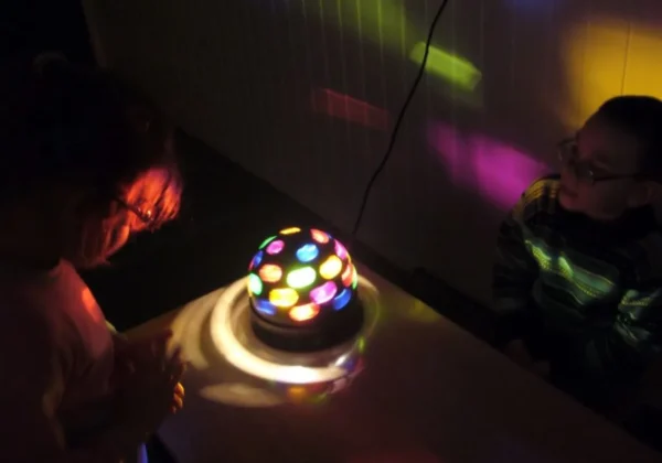 Na zdjęciu widać dwoje dzieci skupionych na kolorowej lampie świetlnej podczas specjalistycznej terapii w Orszymowie.