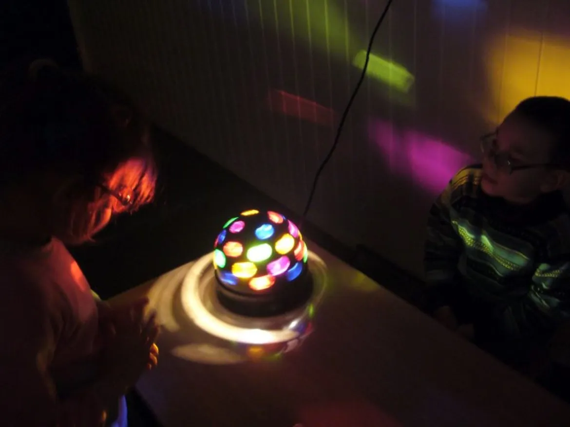 Na zdjęciu widać dwoje dzieci skupionych na kolorowej lampie świetlnej podczas specjalistycznej terapii w Orszymowie.